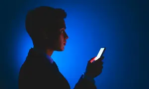 Mężczyzna w garniturze patrzy na jasny ekran telefonu. Dba o ochronę wzroku w telefonie, używając go w ciemności.