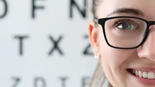 Uśmiechnięta kobieta w okularach przed tablicą Snellena. Kto to jest optometrysta? Specjalista od wzroku, który dba o Twoje oczy.